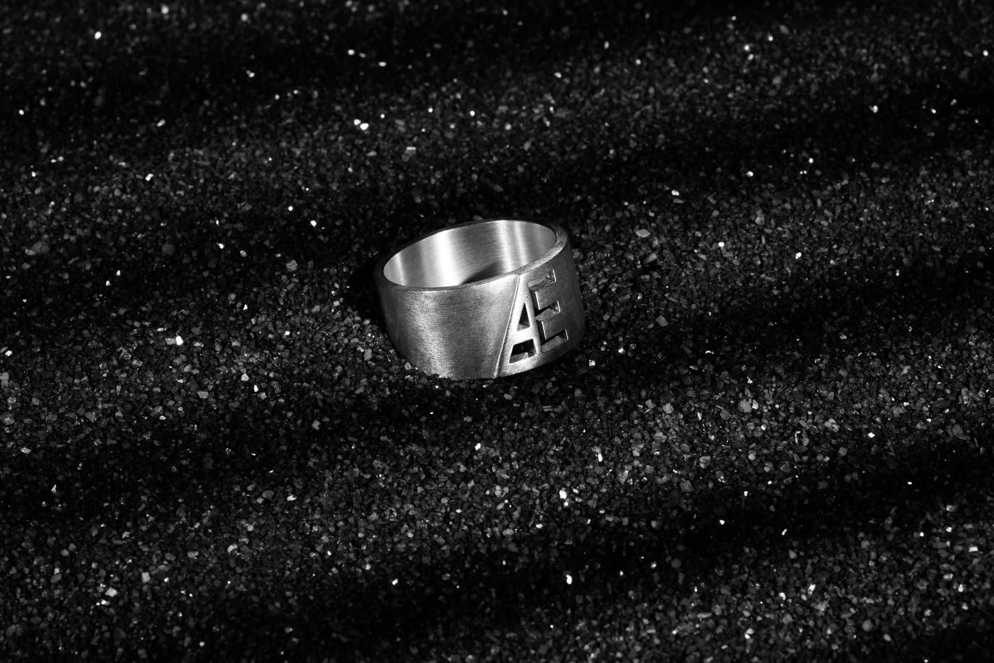 Silver monogram band half buried in black sand