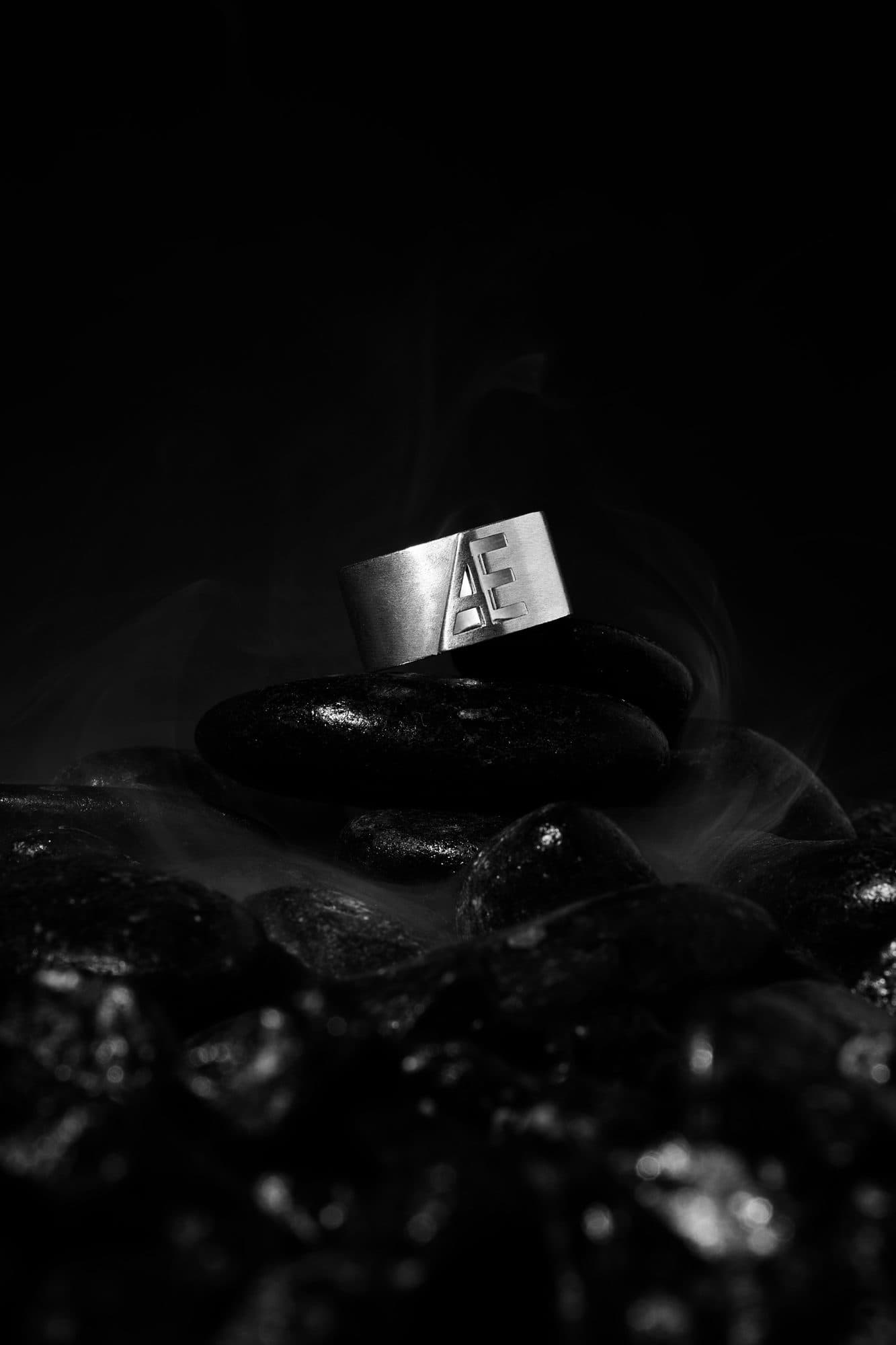 Silver monogram band resting on black stones in smoke