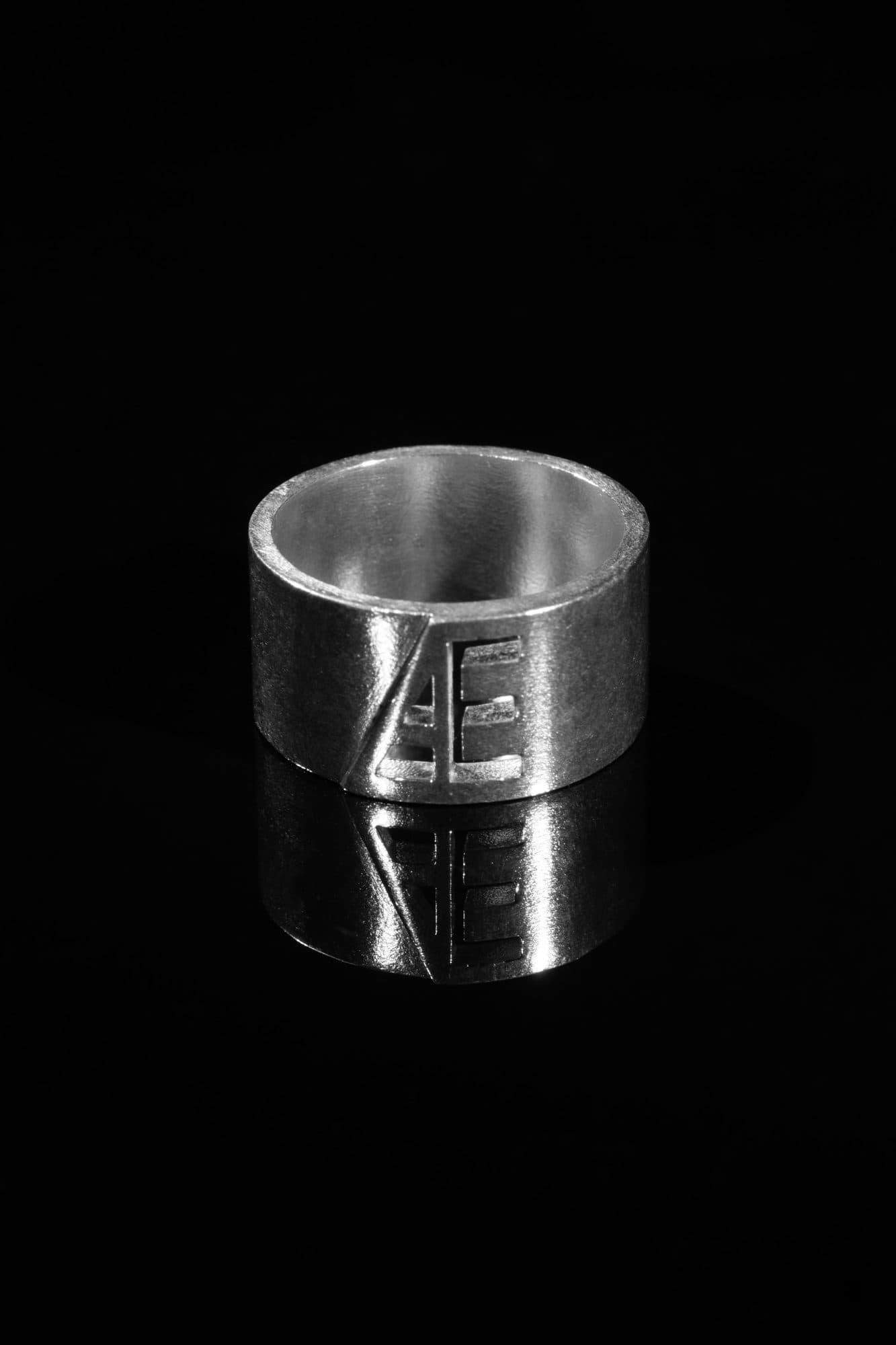 Wide silver band with the Æ monogram on a black mirror surface
