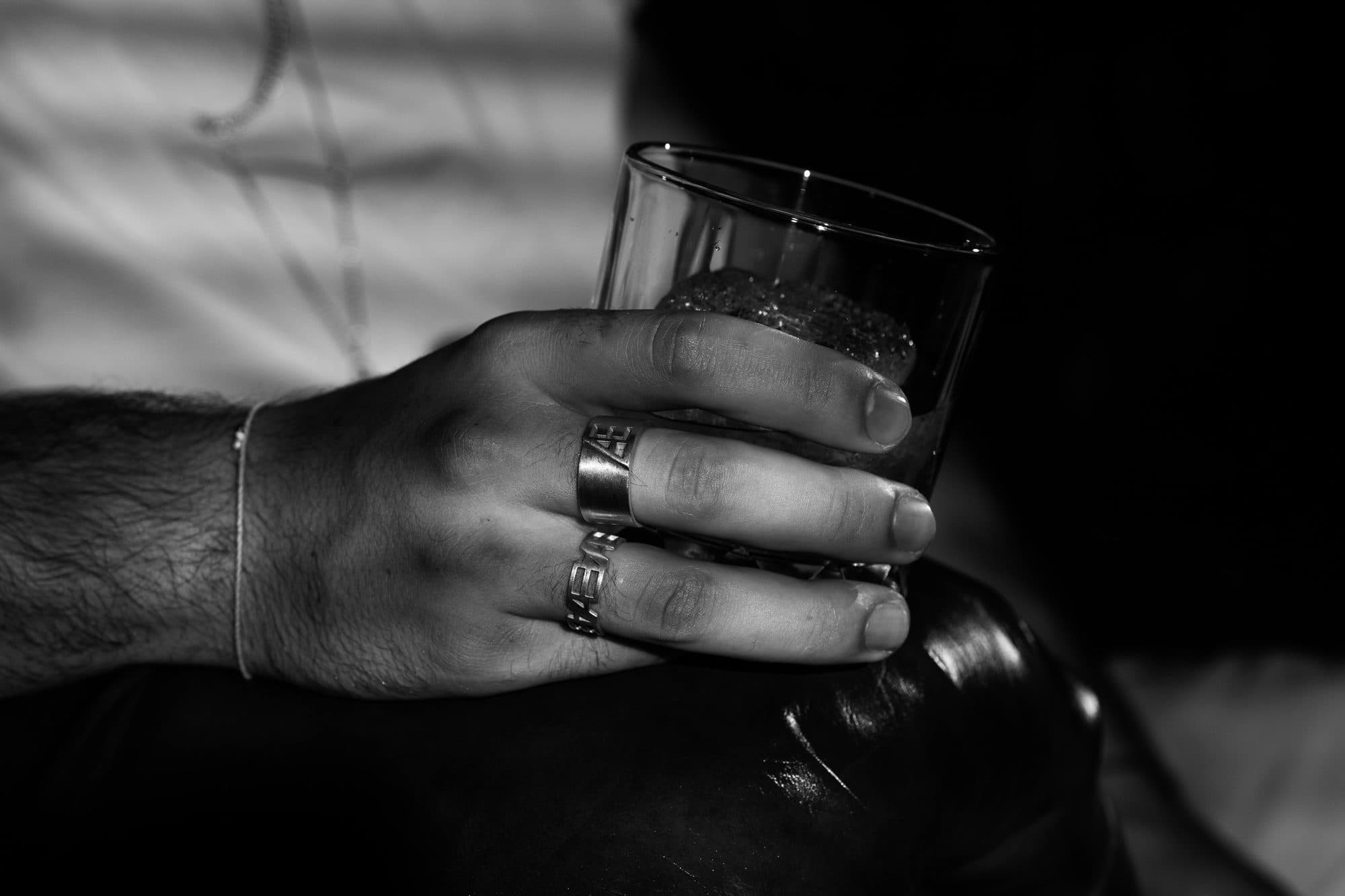 Hand wearing two ÆTHERNO rings holding a glass
